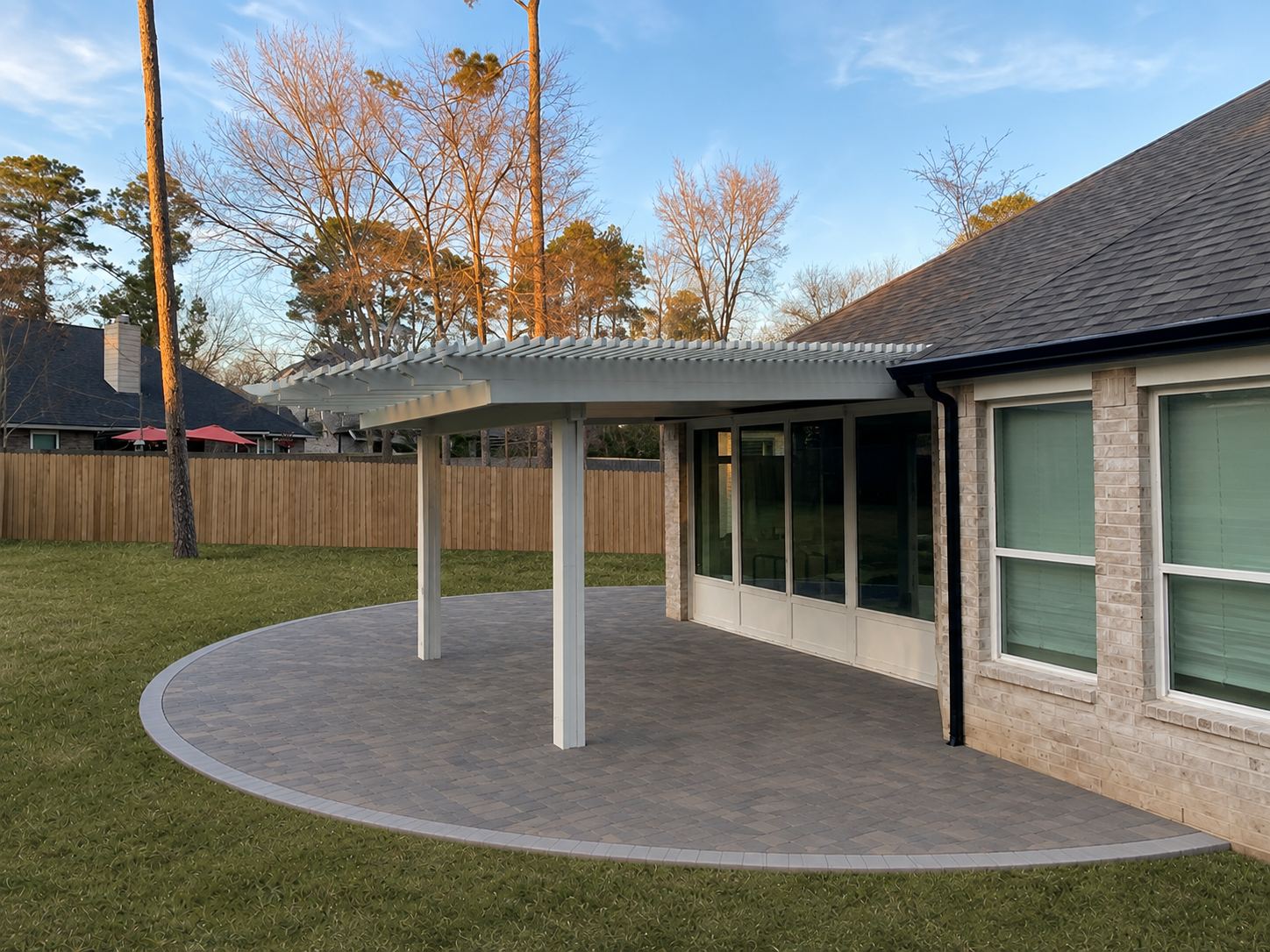 Side view of a hybrid solid-and-lattice patio cover on square columns over a curved paver patio
